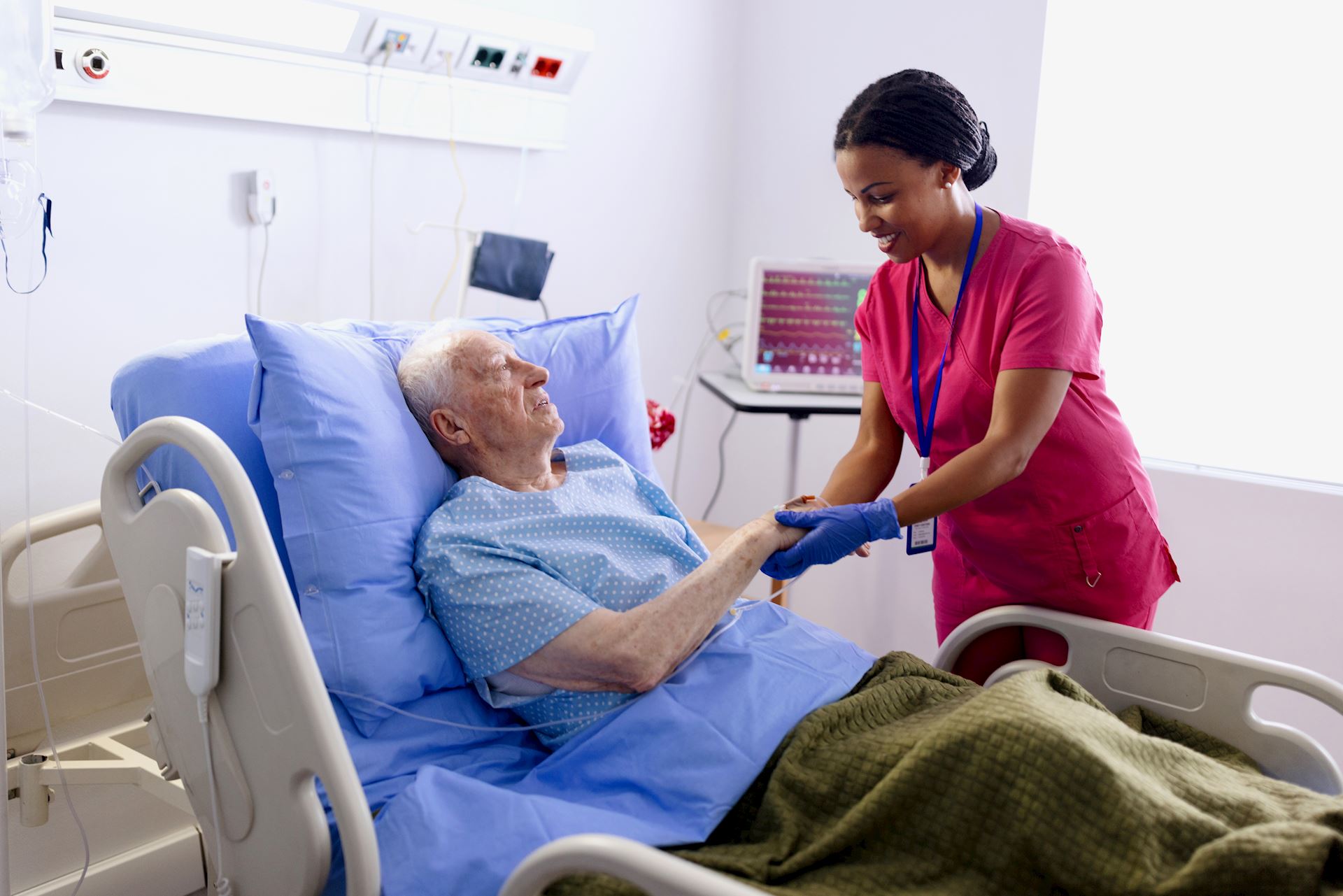 Nurse holding a patients hand in hospital bed